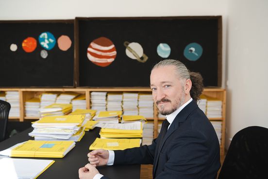 Clemens am Schreibtisch, im Hintergrund Planeten auf Tafeln